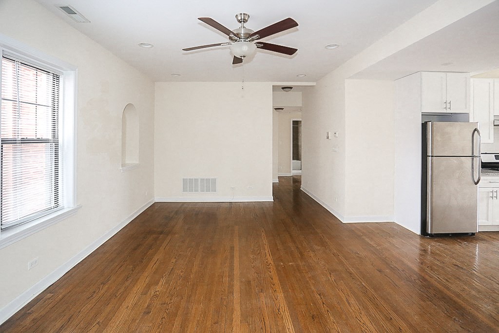 an empty living room with a kitchen and a ceiling fan