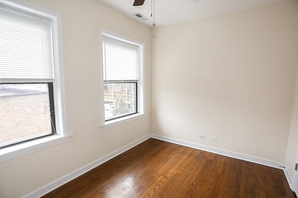 an empty bedroom with two windows and a wooden floor