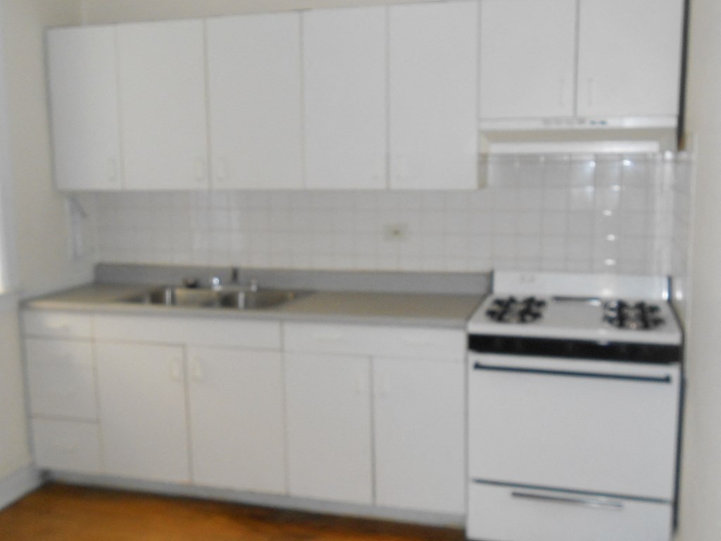 an empty kitchen with white cabinets and a stove and sink
