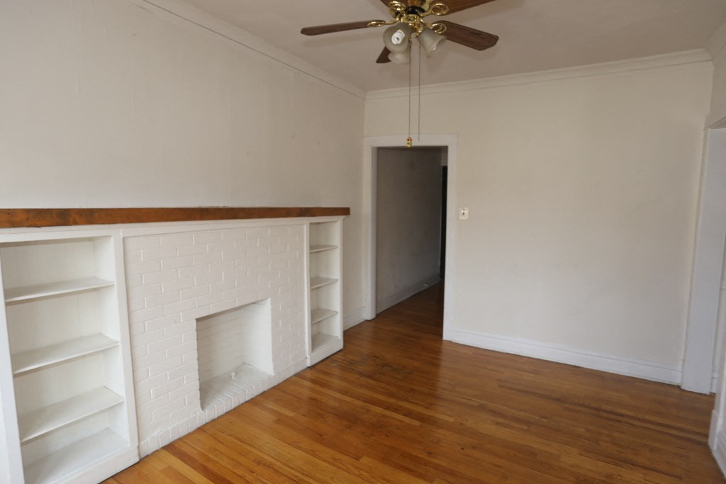 an empty living room with a white brick fireplace and wooden floors