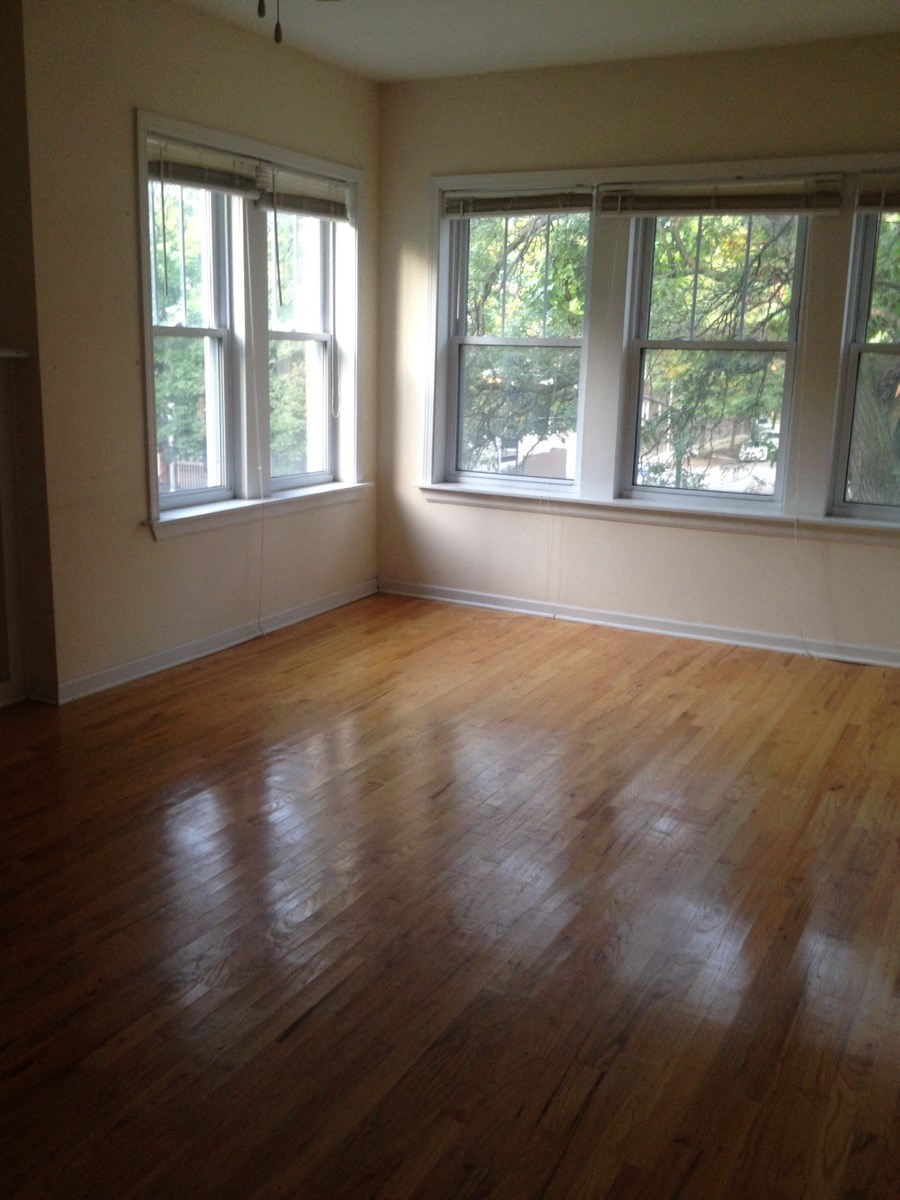 an empty living room with a wooden floor and three windows