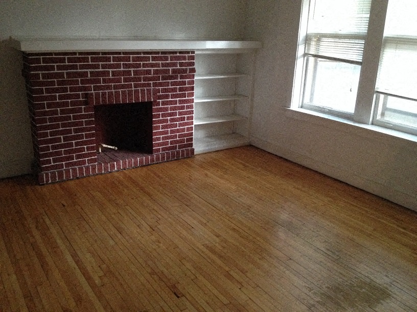 a living room with a brick fireplace and wooden floors