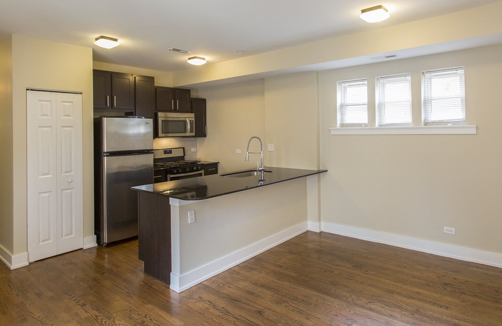 an empty kitchen with a black counter top and a stainless steel refrigerator