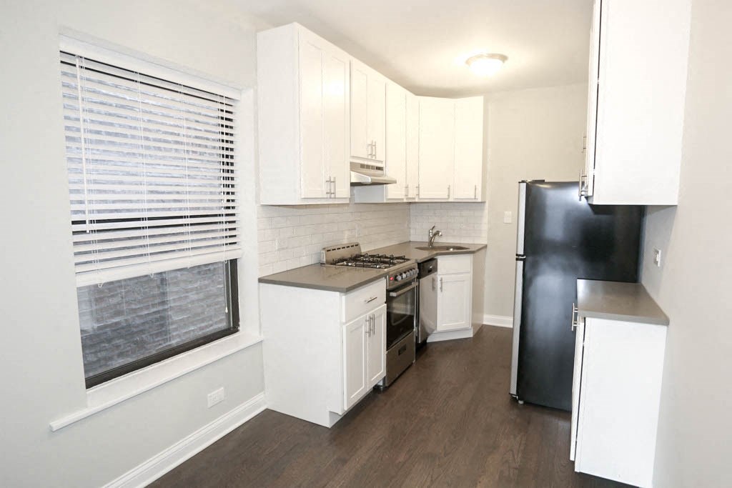 an empty kitchen with white cabinets and a black refrigerator