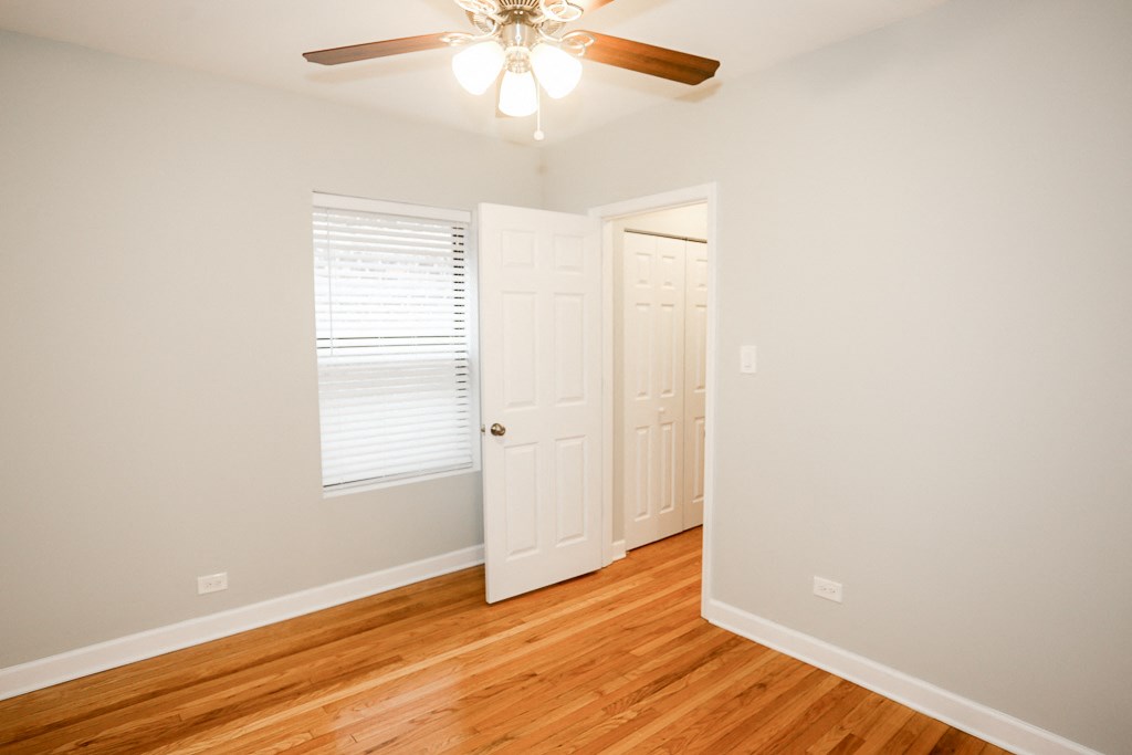 an empty bedroom with wood floors and a ceiling fan