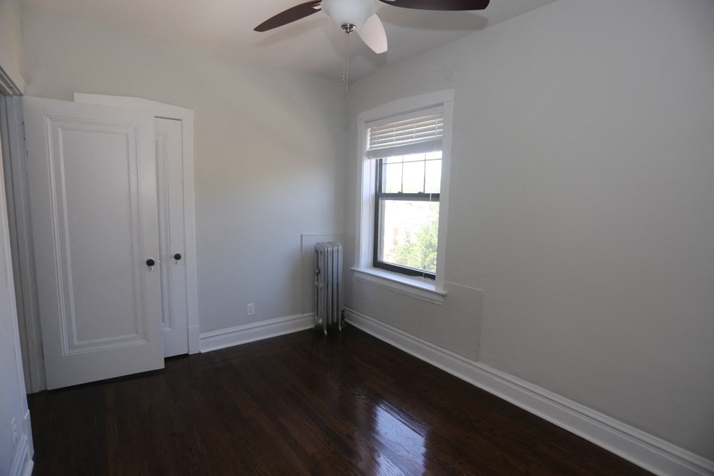 a bedroom with wood floors and a window and a ceiling fan