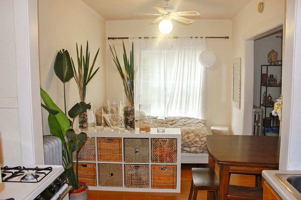 a living room with a bed and a kitchen with a table and a ceiling fan