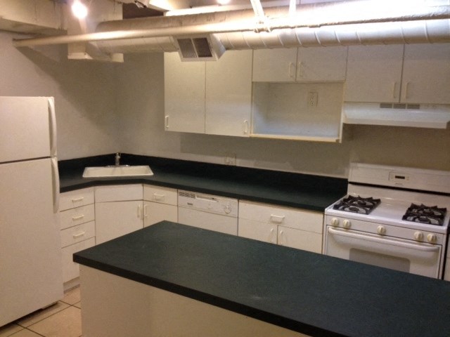 an empty kitchen with white appliances and black counter tops