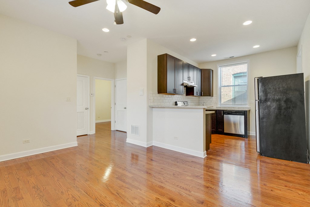 an empty kitchen and living room with wood flooring and a black refrigerator