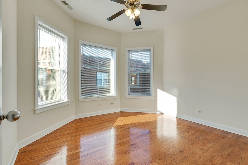 an empty living room with a ceiling fan and three windows