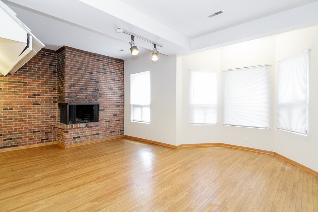 an empty living room with a brick fireplace and wood floors