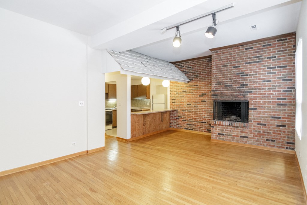 an empty living room with a brick fireplace and a wooden floor