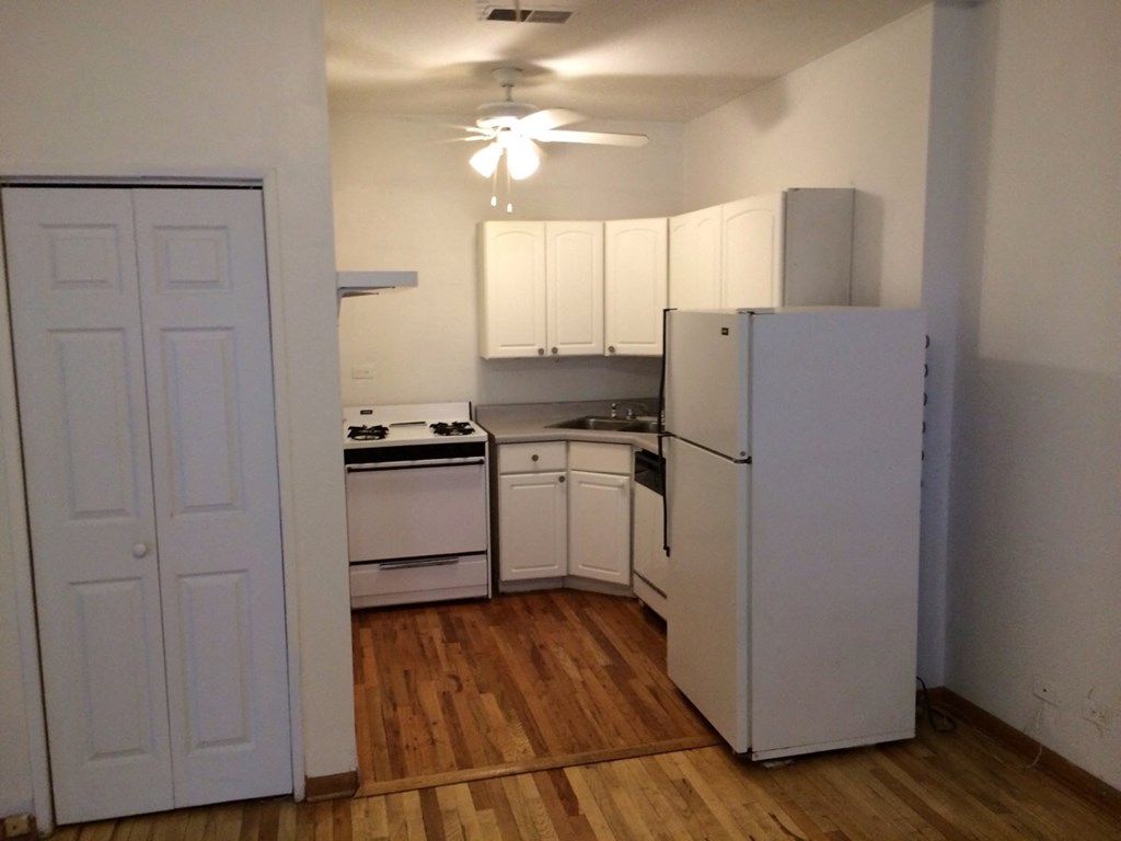 an empty kitchen with white appliances and a refrigerator