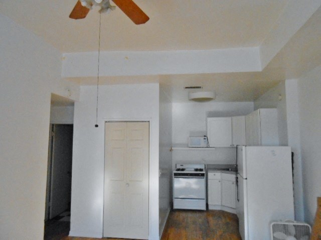 an empty kitchen with white appliances and a ceiling fan