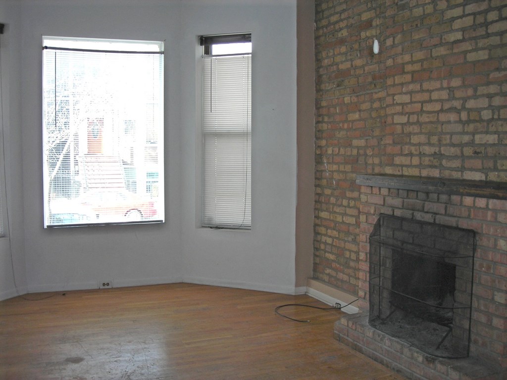 an empty living room with a brick fireplace and two windows