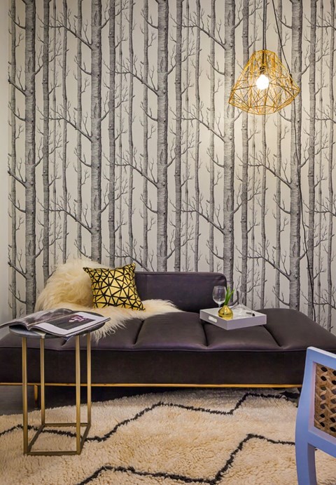A living room with a grey couch and a tree patterned wallpaper.