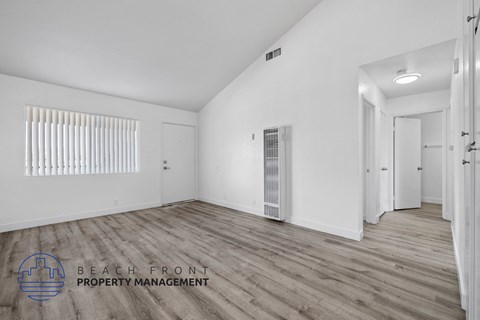 A spacious room with wooden flooring and white walls, with a logo for Beach Front Property Management in the bottom left corner.