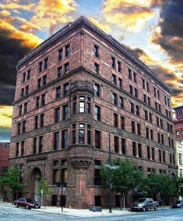 A large red brick building with many windows and a street in front.