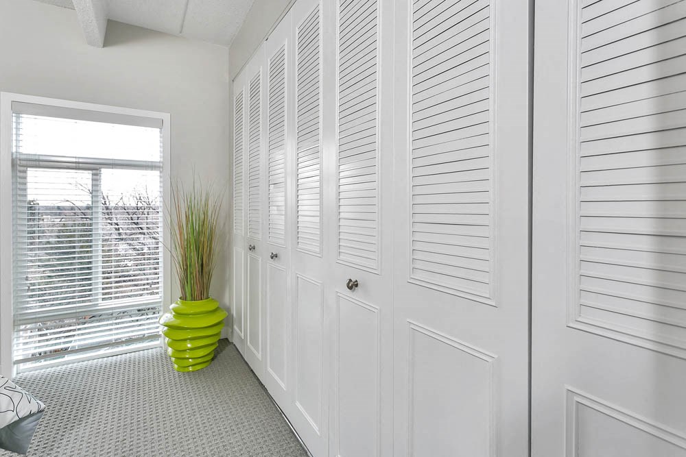 a white closet with white shutters and a yellow vase