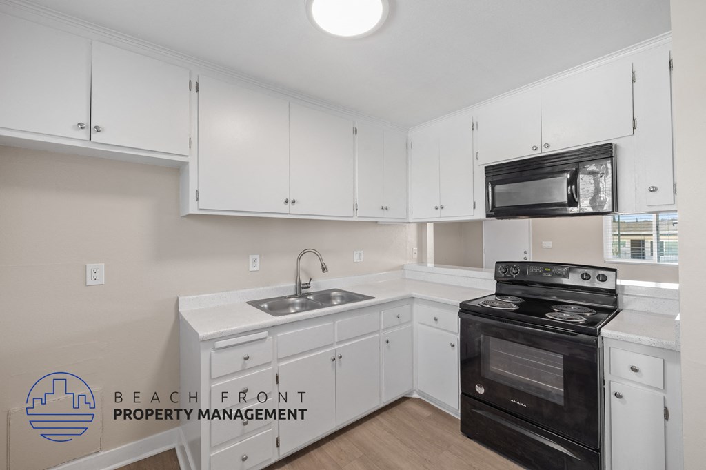 A kitchen with white cabinets and appliances, including a black stove.