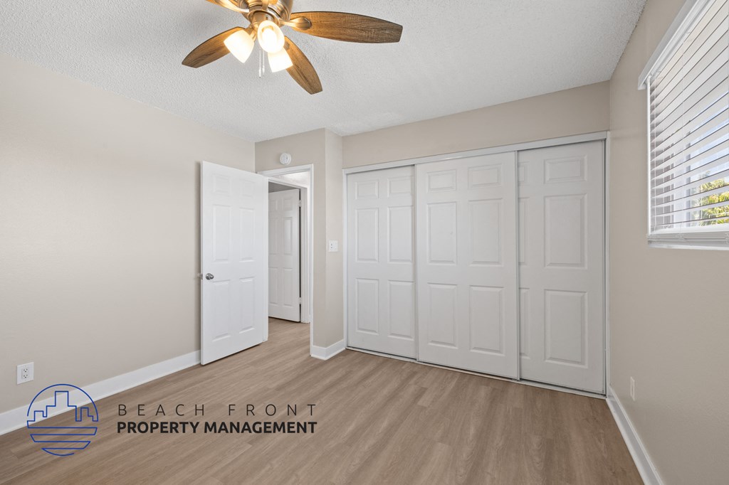 A room with a ceiling fan and a logo for Beach Front Property Management.
