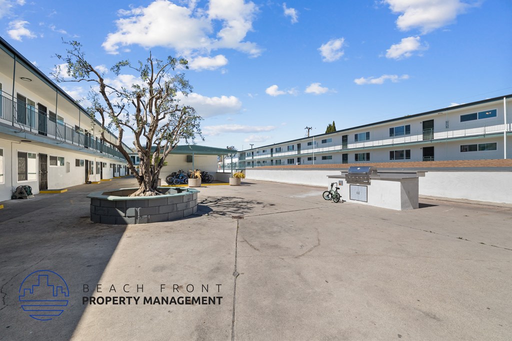 A courtyard with a tree and a bicycle in front of a building with the logo of Beach Front Property Management.