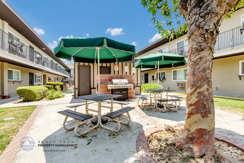 a picnic table with green umbrellas and a grill in the courtyard of a building