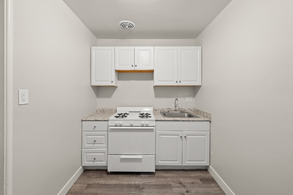 an empty kitchen with white cabinets and a stove and sink