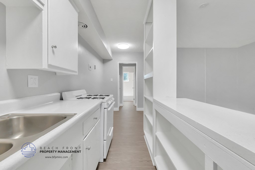 a white kitchen with white cabinets and white countertops and a hallway