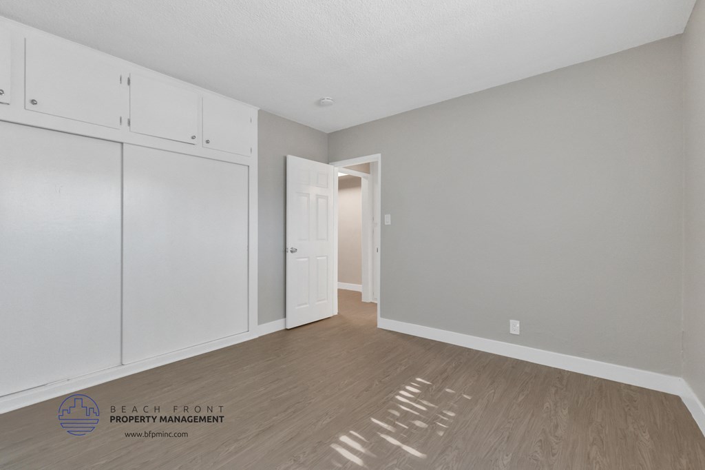 the living room of an apartment with white cabinets and wood flooring