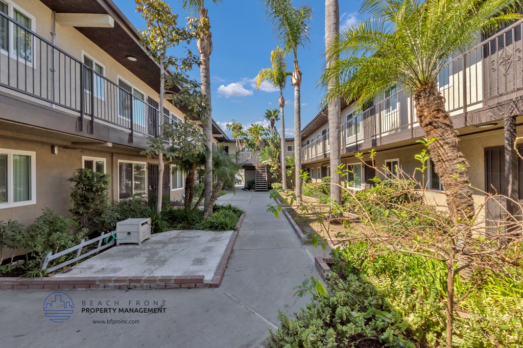 a sidewalk between two apartment buildings with palm trees