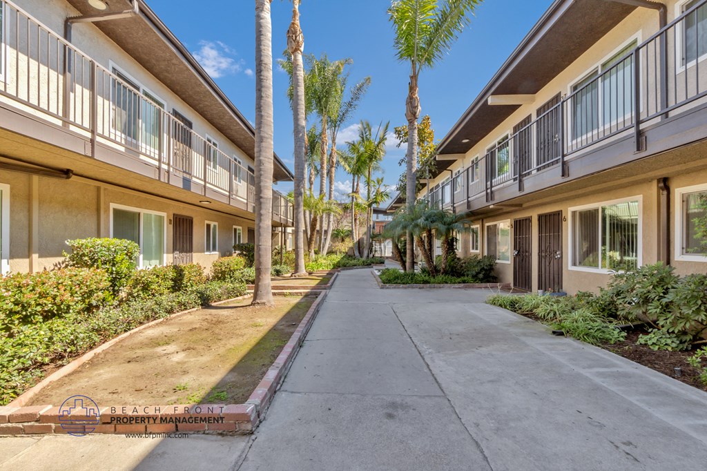 the walkway between two apartment buildings with palm trees