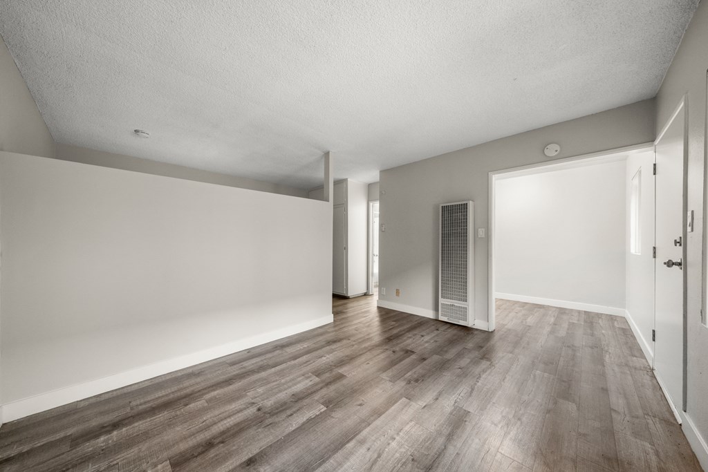 the living room and dining room of an apartment with white walls and wood floors