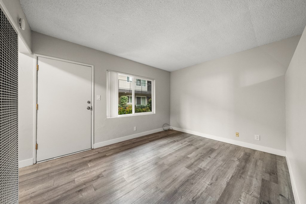 the living room of an apartment with wood flooring and a window
