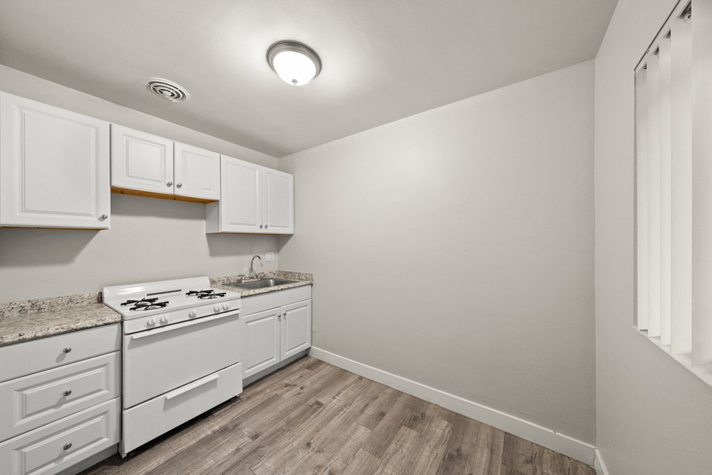 a kitchen with white cabinets and white appliances and wood flooring