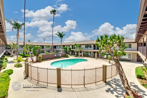 a pool is surrounded by a fence and a building with palm trees