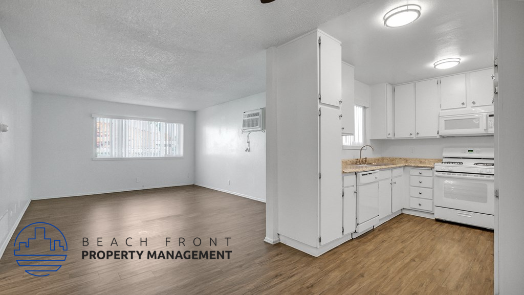 an empty kitchen with white cabinets and white appliances and wood floors