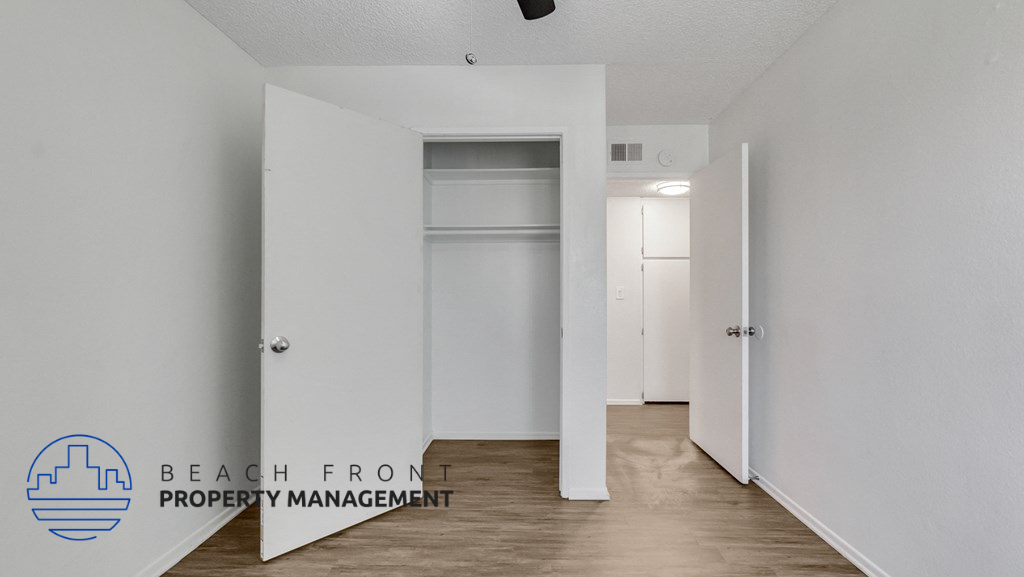 a hallway with white walls and white closets and a hardwood floor and white