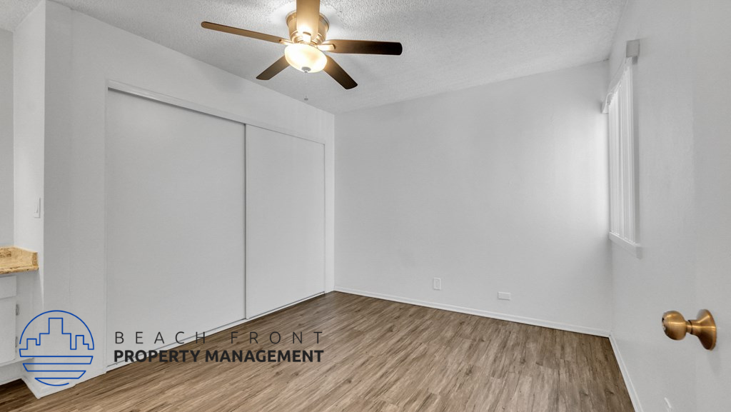 the spacious living room with white walls and wood flooring and a ceiling fan