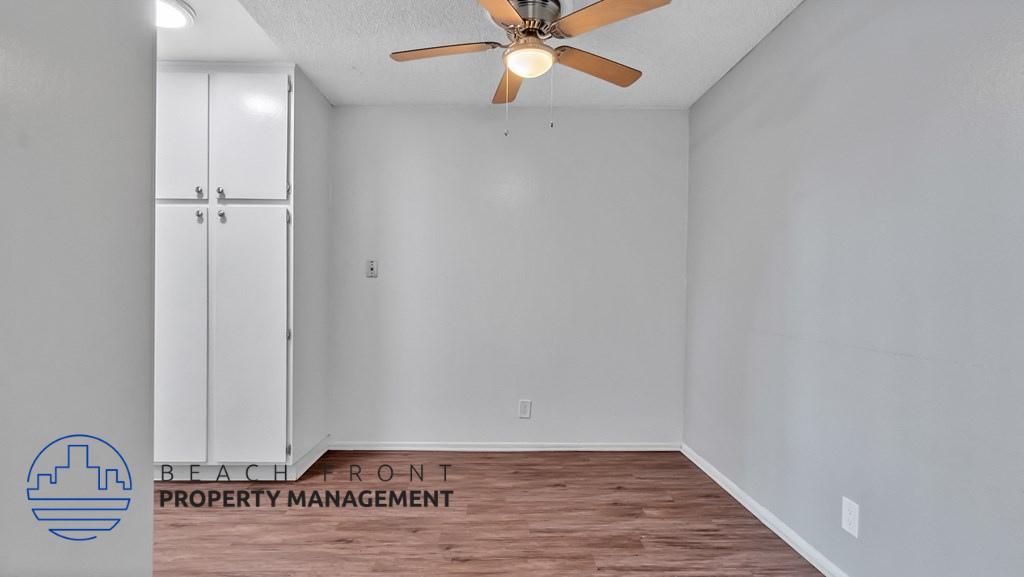 the spacious living room with white walls and a ceiling fan