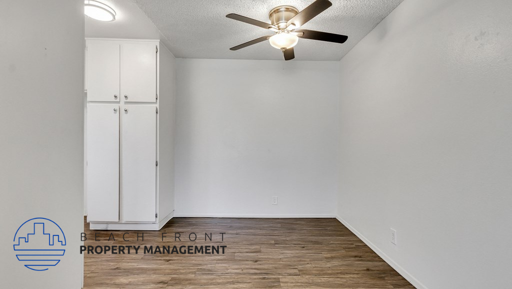 the spacious living room with white walls and a ceiling fan