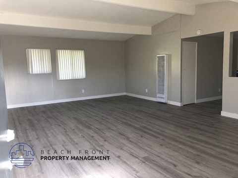 A spacious room with wooden flooring and a logo for Beach Front Property Management in the corner.