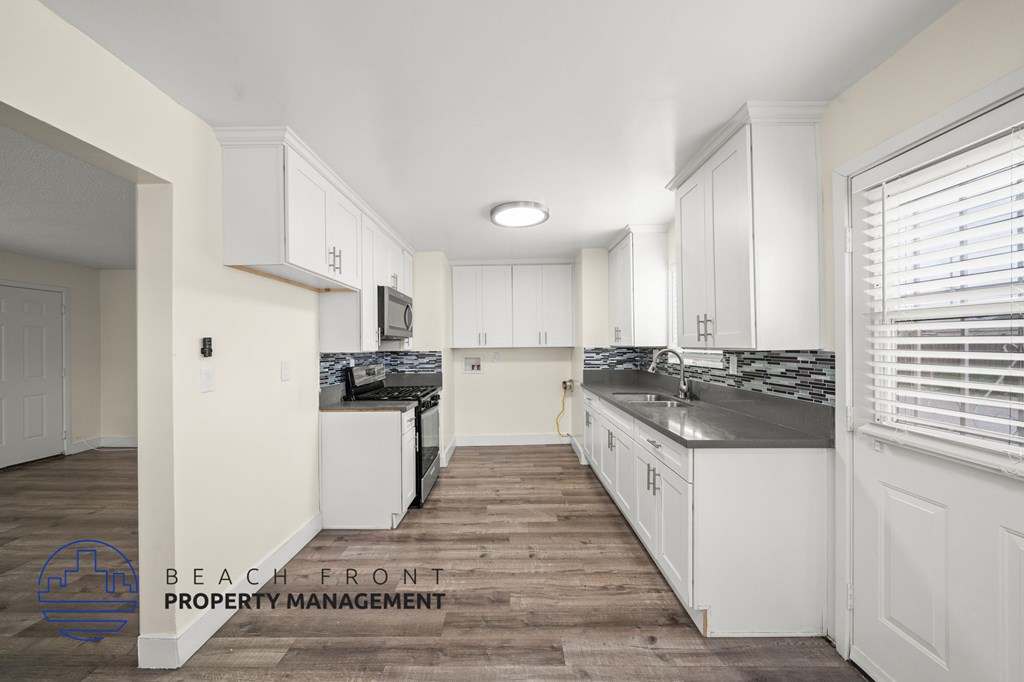 A kitchen with white cabinets and a wooden floor.