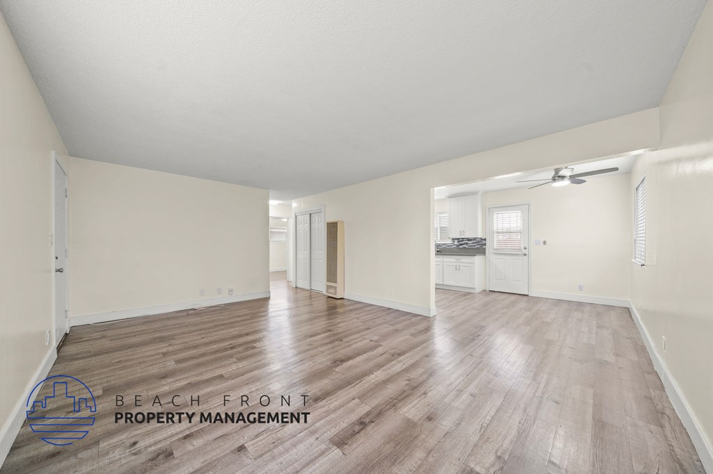 A spacious room with wooden flooring and white walls, with a logo for Beach Front Property Management in the bottom left corner.