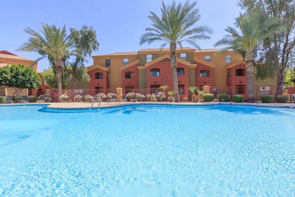 a large swimming pool with palm trees and apartments in the background
