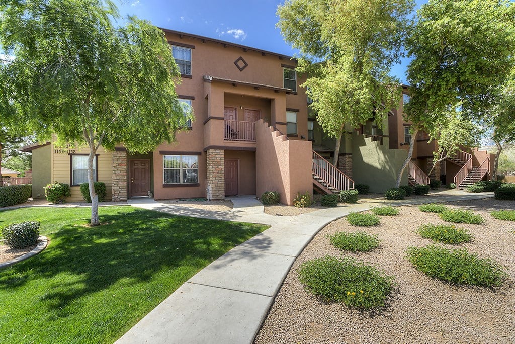 an apartment building with a sidewalk and trees in front of it