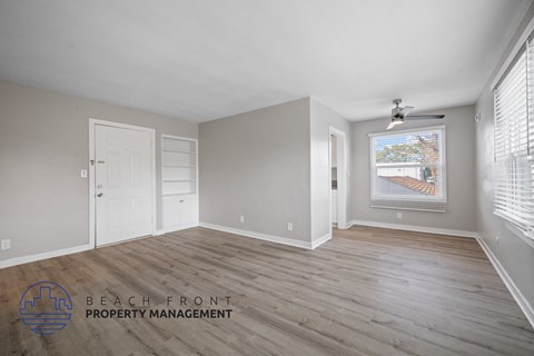 A spacious room with wooden flooring and a ceiling fan, with a window showing a view of a wooden deck.