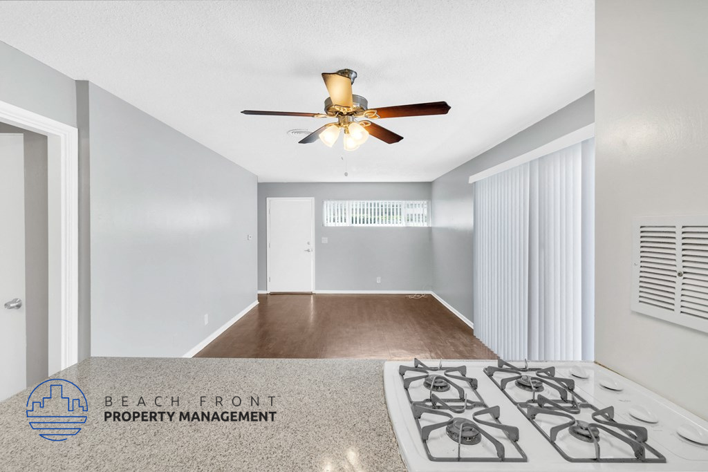 an empty living room with a ceiling fan and a kitchen