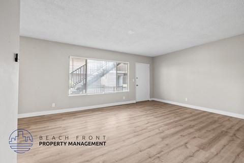 A spacious room with wooden flooring and a large window overlooking a balcony.
