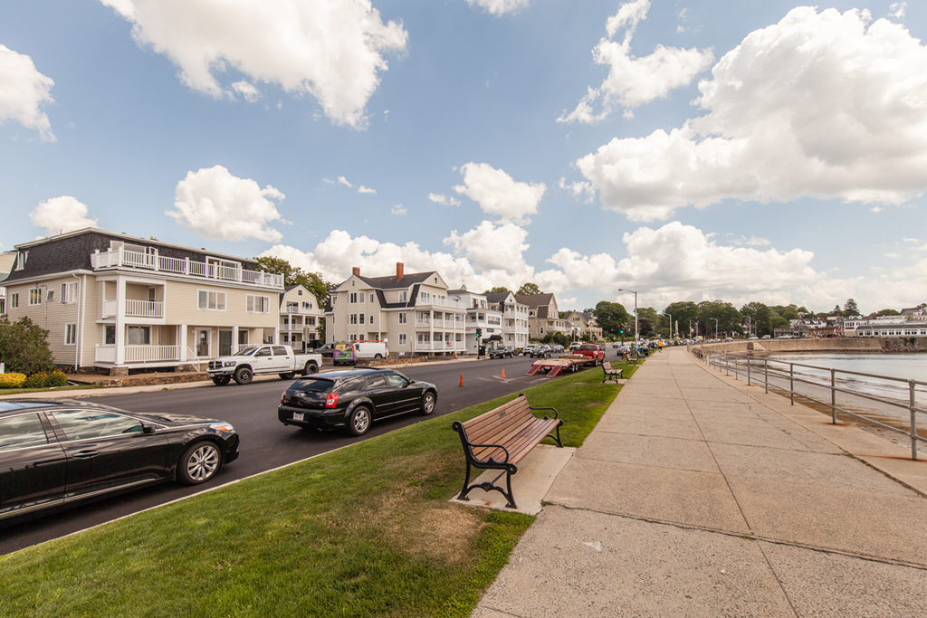 a bench on a sidewalk next to a body of water with cars on the street